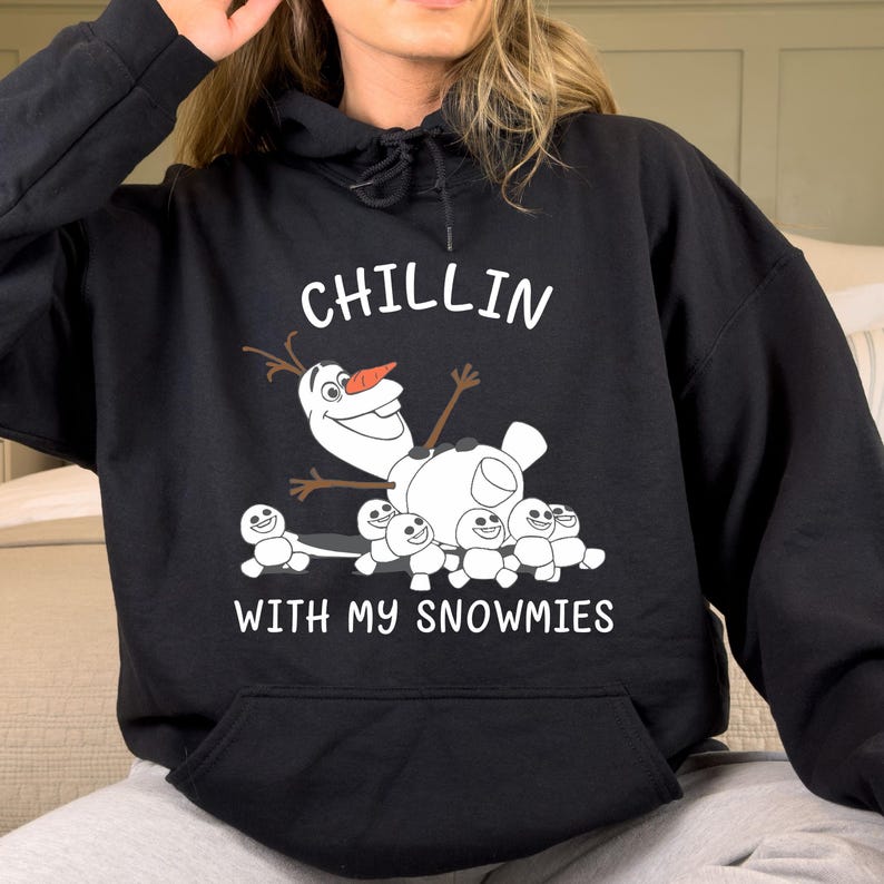 A person wearing a black hoodie with a graphic of Olaf, the main character from the Disney movie Frozen, and the text "Chillin with my snowmies" printed on it.