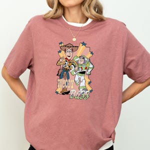 A woman wearing a pink t-shirt with a graphic of Woody and Buzz Lightyear from the Toy Story movie.