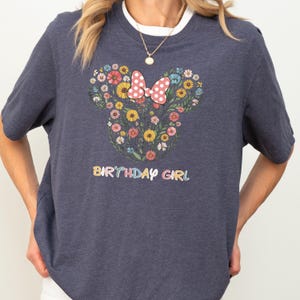 A person wearing a gray t-shirt with a graphic design of a flowery Minnie Mouse and the text "BIRTHDAY GIRL" printed on it.