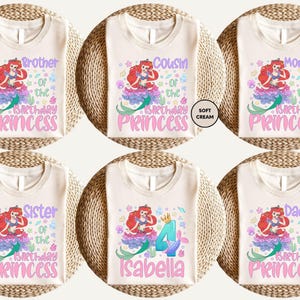 six white t-shirts with different designs and text related to birthday celebrations. The t-shirts feature a mermaid character and the names of the birthday person, such as "Brother of the Princess", "Cousin of the Birthday Princess", "Mommy of the Birthday Princess", "Sister of the Birthday Princess", "Daddy of the Birthday Princess", and "Isabella". The text on the t-shirts is colorful and includes the names of the birthday person and the character they are associated with.