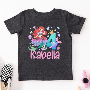 A gray t-shirt with a mermaid character and the number 4 printed on it, along with the name "Isabella" written below.