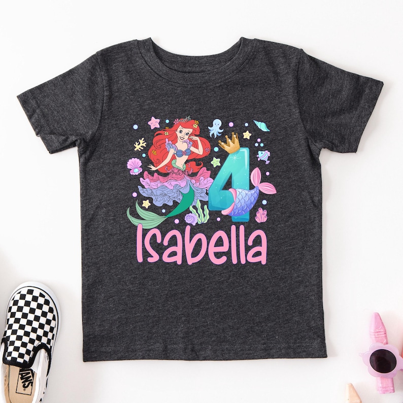 A gray t-shirt with a mermaid character and the number 4 printed on it, along with the name "Isabella" written below.