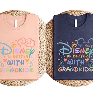 two Disney-themed t-shirts, one pink and one blue, with the text "Disney is better with Grandkids" printed on them.