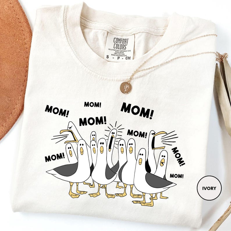 A white t-shirt with a graphic design of a group of seagulls and the text "MOM! MOM! MOM!" printed on it.
