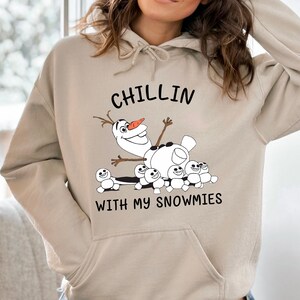 A person wearing a beige hoodie with a graphic design featuring a cartoon character and text.