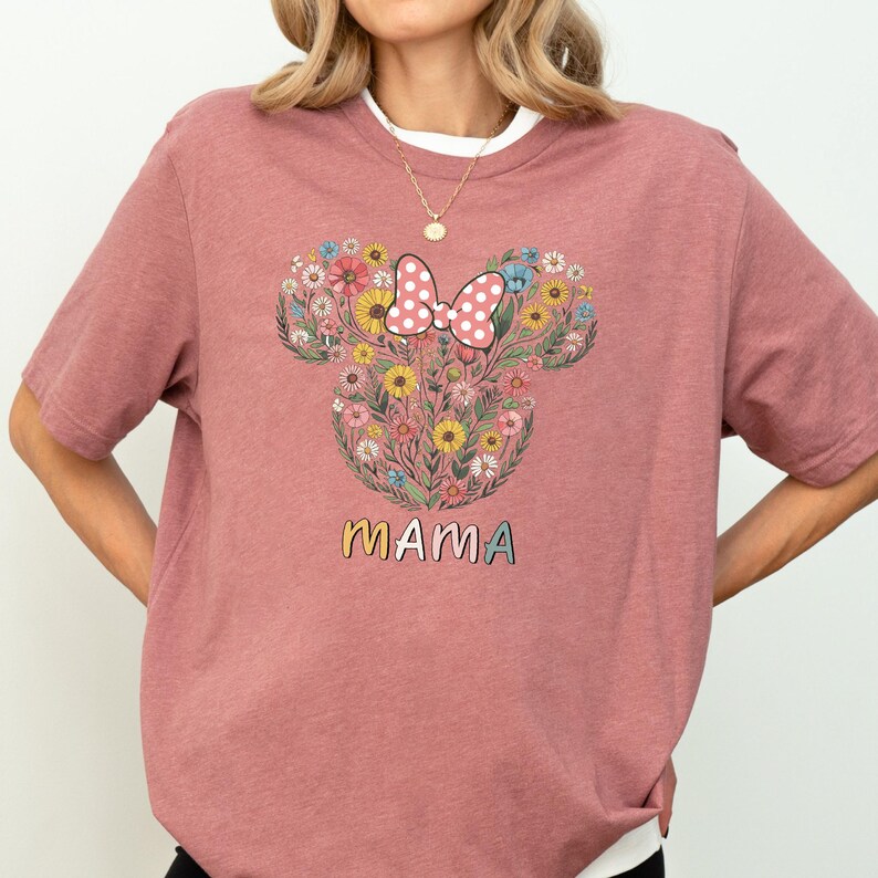 A woman wearing a pink t-shirt with a floral design and the word "mama" printed on it.