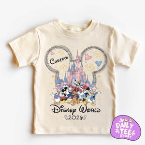 A white t-shirt with a Disney World-themed graphic design featuring Mickey Mouse, Minnie Mouse, Donald Duck, and Goofy, along with a castle and fireworks.