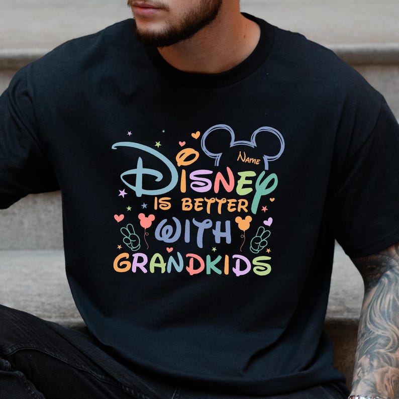 A black t-shirt with a colorful graphic design that says "Disney is better with grandkids" and includes various Disney-themed elements such as Mickey Mouse ears and hearts.