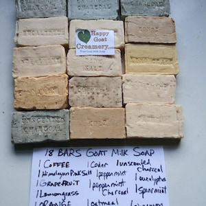 May include: An assortment of 18 bars of goat milk soap in various colors and scents, including charcoal, lavender, and coffee. The bars are rectangular and stamped with the scent name. A handwritten list details the soap varieties.