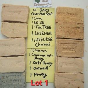 May include: Ten rectangular bars of goat milk soap arranged in two columns with a yellow note in the center. The note lists the scents: Clove, Anise, Tea Tree, Lavender, Lavender Charcoal, Cinnamon, Cinnamon Oat Honey, Oat Honey, Oatmeal, and Honey.