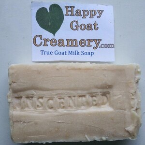 May include: A rectangular bar of unscented goat milk soap. The soap is a light beige color with the word "UNSCENTED" embossed on the surface. A white label above the soap reads "Happy Goat Creamery.com True Goat Milk Soap."