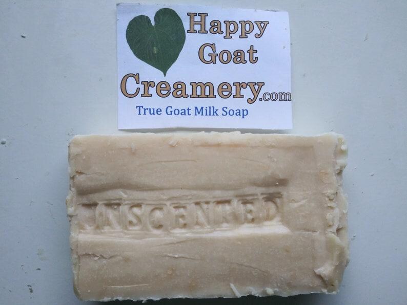 May include: A rectangular bar of unscented goat milk soap. The soap is a light beige color with the word "UNSCENTED" embossed on the surface. A white label above the soap reads "Happy Goat Creamery.com True Goat Milk Soap."