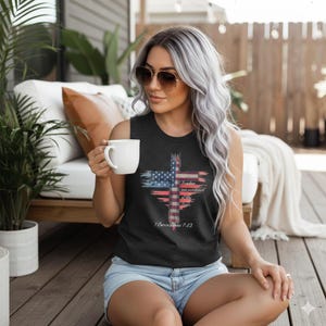 May include: A charcoal gray sleeveless shirt featuring a cross design with the American flag incorporated. The cross design includes the words "Freedom was purchased with a price" and the Bible verse 1 Corinthians 7:23.