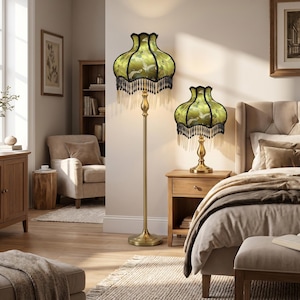 May include: A floor lamp and a matching table lamp, both featuring a brass-toned metal base and a bell-shaped green fabric shade with a bird pattern, finished with a decorative black beaded fringe trim along the bottom edge of the lampshades.