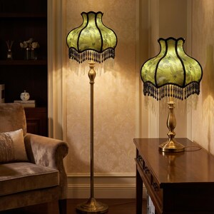 May include: A floor lamp and a matching table lamp, both featuring brass-toned metal stands and bell-shaped shades in light green with a floral pattern. The shades are trimmed with black fabric edges and decorative hanging black beaded fringe.