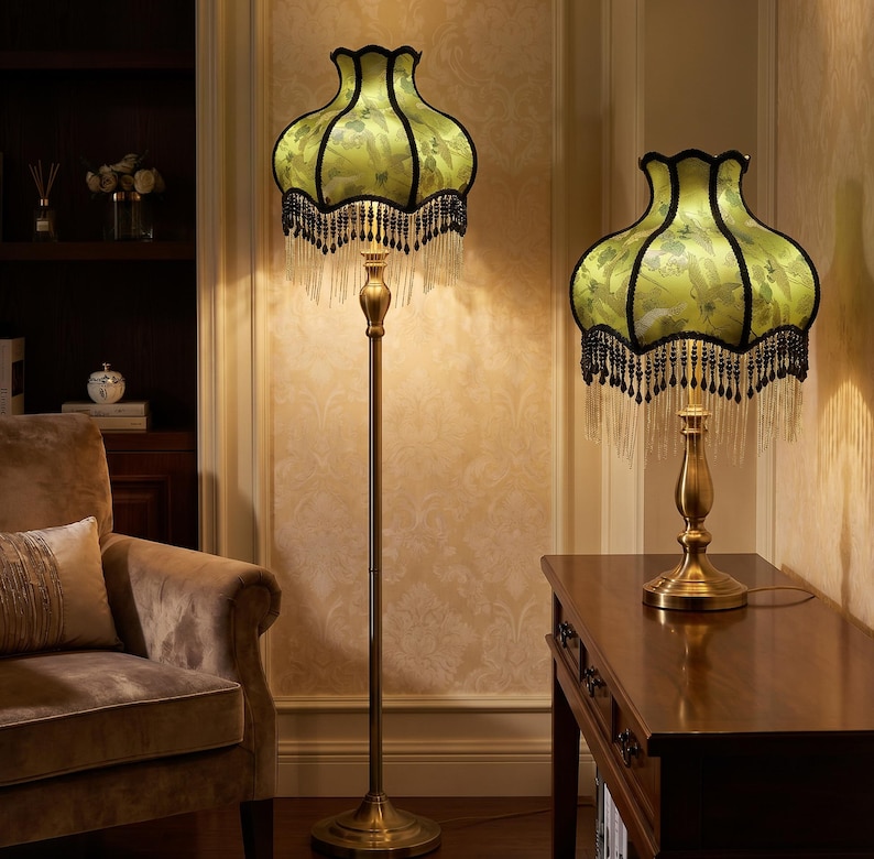 May include: A floor lamp and a matching table lamp, both featuring brass-toned metal stands and bell-shaped shades in light green with a floral pattern. The shades are trimmed with black fabric edges and decorative hanging black beaded fringe.