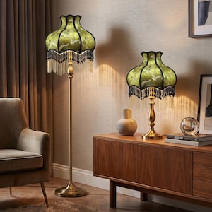 May include: A floor lamp and a matching table lamp, both featuring a brass-toned metal stand and a bell-shaped green fabric shade with a bird pattern, black trim, and long hanging black and gold fringe tassels around the bottom edge.