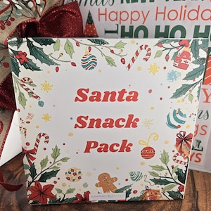 May include: A white Santa Snack Pack box with red text and Christmas-themed illustrations. The box is decorated with candy canes, ornaments, and a gingerbread man. A red bow and other holiday-themed items are in the background.