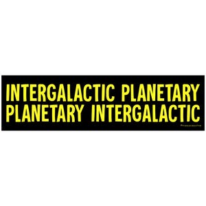 May include: A black rectangle with the words "INTERGALACTIC PLANETARY PLANETARY INTERGALACTIC" in yellow block letters. The text is centered and stacked in two rows. The background is white.