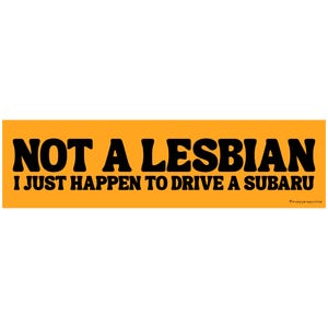 May include: An orange bumper sticker with black text that reads "NOT A LESBIAN I JUST HAPPEN TO DRIVE A SUBARU". The sticker has a rectangular shape and is set against a white background.