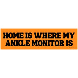 May include: An orange rectangle with the text "HOME IS WHERE MY ANKLE MONITOR IS" in bold, black letters. The phrase is centered, and the overall design is simple and eye-catching. The bottom right corner has a small text that reads "@moodygirlshop".