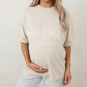 May include: A beige t-shirt with the text "coconut coffee mockups" in a script font. The shirt is a neutral color and has short sleeves. The model is wearing gray sweatpants.