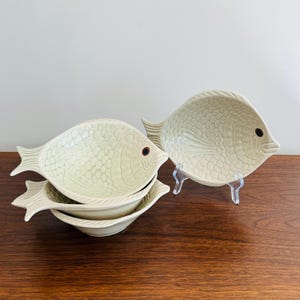 May include: A set of three ceramic mugs with a speckled, matte finish. The mugs are in shades of cream, light gray, and dark gray. Each mug has a simple, minimalist design, perfect for coffee or tea.