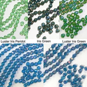 May include: Assortment of iridescent glass beads in various shades of green and blue. The beads are faceted and have a lustre finish.