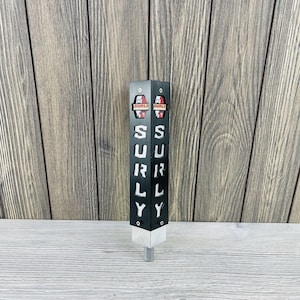 Könnte beinhalten: Schwarzer und silberner Bierhahn-Griff mit dem Wort "SURLY" aus dem schwarzen Körper ausgeschnitten. Die Oberseite des Griffs hat zwei rot-weiße "SURLY"-Logos. Der Zapfhahngriff ist aus Metall gefertigt und für die Verwendung mit einem Bierfass konzipiert.