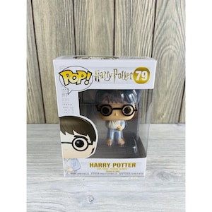 May include: A Harry Potter Pop! Vinyl figure, number 79, in its original packaging. The figure depicts Harry Potter wearing glasses and pajamas. The box features the Pop! logo and the Harry Potter title.