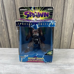 May include: A boxed Todd McFarlane's Spawn Mutant Spawn Ultra-Action Figure. The figure is a special edition, featuring a detailed, dark brown and black design with green accents. The packaging is blue with lightning bolt graphics.