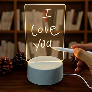 May include: A clear acrylic LED night light with the words "I Love You" written on it in white. The light sits on a light blue base and is illuminated. A white pen is near the acrylic.