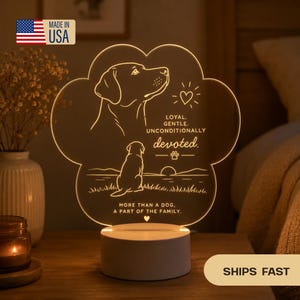 May include: A paw-shaped LED night light with a dog silhouette and the words "LOYAL, GENTLE, UNCONDITIONALLY devoted. MORE THAN A DOG, A PART OF THE FAMILY." The base is white, and the light glows with a warm, inviting hue. Made in the USA.