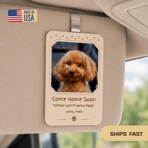 May include: A rectangular light-colored wooden car visor clip featuring a photo of a brown poodle. The text reads: Come Home Soon, Dinner won't serve itself. Love, Max. A small paw print icon is at the bottom, and paw prints border the top edge.