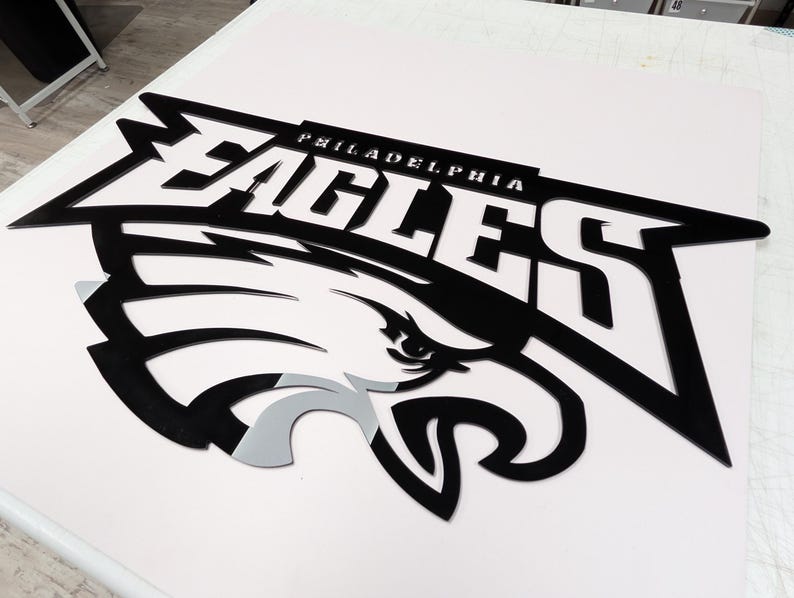 Puede incluir: Un logotipo en blanco y negro de los Philadelphia Eagles, con el nombre del equipo y una cabeza de &aacute;guila estilizada. La palabra "PHILADELPHIA" est&aacute; encima de la palabra "EAGLES". La cabeza del &aacute;guila tiene acentos grises y blancos.