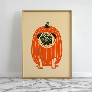 Könnte beinhalten: Ein gerahmter Kunstdruck mit einer stilisierten Illustration eines Mopses in einem großen orangefarbenen Kürbis. Der Mops hat schwarze Gesichtszüge und ist mittig im Kürbis platziert, der mit vertikalen weißen Linien versehen ist.