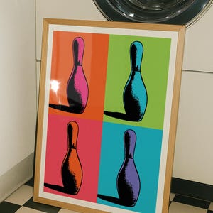 May include: A framed rectangular wall art print featuring a four-panel grid design. Each panel displays a single bowling pin silhouette in a different colour against a vibrant background of orange, lime green, pink, and bright blue, with black shadows.