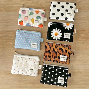 May include: Six rectangular fabric zip pouches with various patterns including strawberries, polka dots, daisies, and leopard print. Each pouch features a small white label with the text "beshie Handmade" stitched on the front right side.