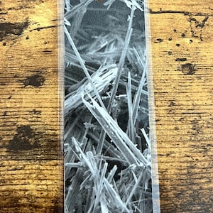 May include: A rectangular bookmark with a black and white abstract image of crystalline structures. The bookmark has a silver tassel attached at the top. The background is a wooden surface.