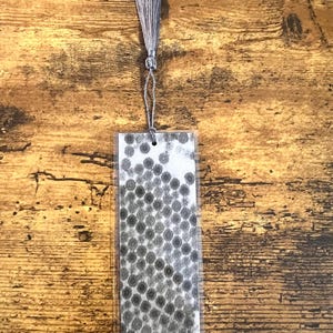 May include: A rectangular bookmark with a gray tassel. The bookmark features a black and white image of a microscopic view of a biological structure. The tassel is attached to the top of the bookmark with a silver-colored string.