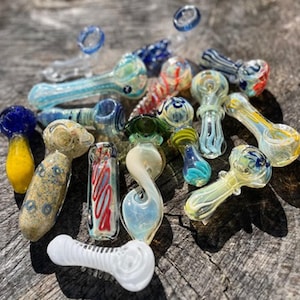 May include: A collection of colorful glass pipes in various shapes and designs. The pipes feature a range of colors, including blue, yellow, red, and clear, with decorative patterns. Some have curved stems, while others are straight.