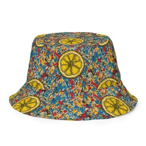 May include: A bucket hat with a bright, colourful design. The hat features a pattern of yellow lemon slices on a background of blue, red, and yellow paint splatters. The hat is a casual accessory.