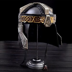 Peut inclure: Casque en cuir noir avec des détails argentés et dorés. Le casque présente une bande décorative avec des motifs géométriques et un dessus tressé. Il est exposé sur un support en métal noir.