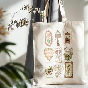 May include: Cream-colored tote bag featuring various framed illustrations. Designs include a tulip, lamp, jar of cookies, heart, flowers, a hen in a basket, teacup, teapot, and lemons. The bag is made of a sturdy fabric.