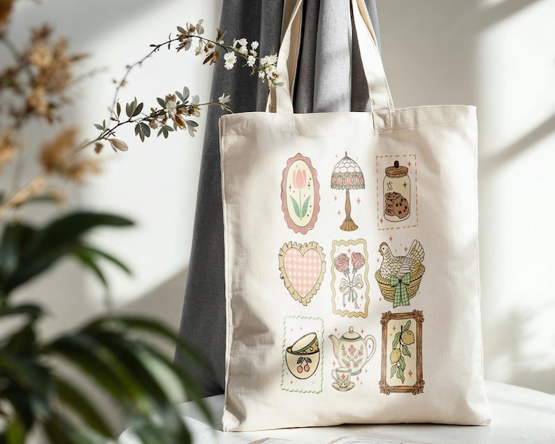 May include: Cream-colored tote bag featuring various framed illustrations. Designs include a tulip, lamp, jar of cookies, heart, flowers, a hen in a basket, teacup, teapot, and lemons. The bag is made of a sturdy fabric.