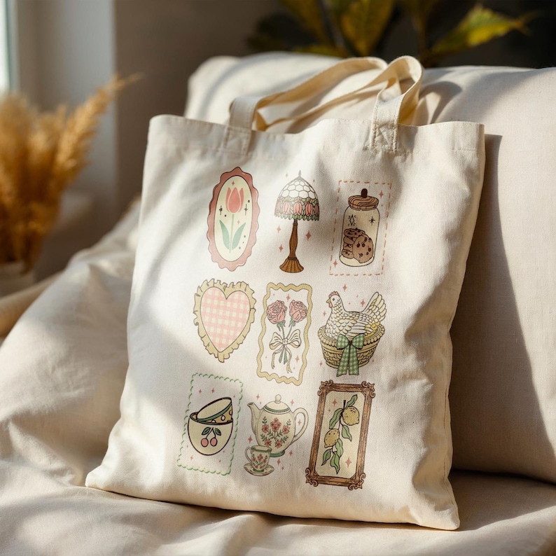 May include: Cream-colored tote bag featuring various framed illustrations. Designs include a tulip, a lamp, a jar of cookies, a heart, roses, a chicken in a basket, a teacup, a teapot, and lemons. The bag has two handles.