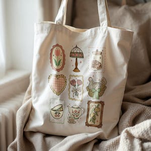 May include: Cream-colored tote bag featuring a collection of vintage-style illustrations. The designs include a tulip, a lamp, cookies in a jar, a heart, roses, a chicken in a basket, teacups, a teapot, and lemons. The bag has two handles.
