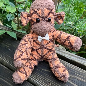 Mono de peluche suave hecho a mano: color naranja con rayas entrecruzadas marrones.