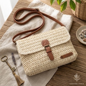 May include: A rectangular crossbody bag made of woven beige straw material. The bag features a long brown adjustable shoulder strap, a front flap closure secured with a brown faux leather buckle strap, and a small brown rectangular accent patch.
