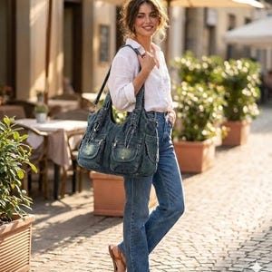May include: A denim tote bag with multiple front pockets and a shoulder strap. The bag is a faded blue color and has a casual, worn look. The person is wearing blue jeans and a white shirt.
